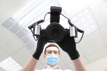 A camera with a ring flash in the hands of a doctor. Doctor in a medical mask. Hands in protective black gloves. Modern dental office. Bottom view. The camera is out of focus.