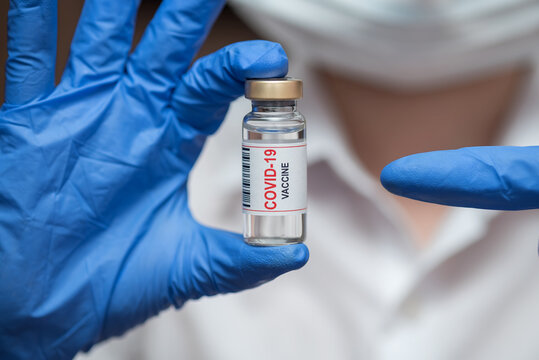 Vaccine in ampoule. From the coronavirus. The doctor keeps in blue gloves.