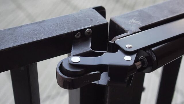 Hydraulic door closer closes the iron door in the yard. The black metal gate closes in slow motion. Wicket close up