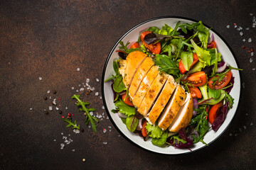 Fresh salad with baked chicken breast at dark kitchen table. Healthy food, clean eating concept. Top view image.