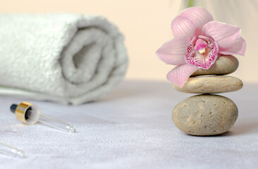 Composition of natural stones, rolled white towel and pink orchid flower. Beauty spa concept.