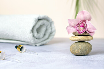 Fototapeta na wymiar Composition of natural stones, rolled white towel and pink orchid flower. Beauty spa concept.
