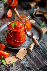homemade red tomato sauce in glass jar on metal plate on wooden table with basil leaves