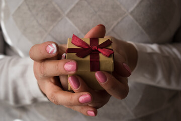 Woman hands holding a small present box with red ribbon over. Valentine gift box.