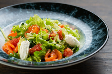 Greek salad of tomatoes, pickled peppers, cucumbers, lettuce and feta cheese. greek salad with olives and white sesame seeds on a blue marble plate