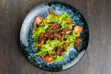 salad of stewed beef, lettuce, pickled peppers and cherry tomatoes. beef salad on a blue marble plate. view from above