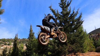 Professional dirt bike motocross rider performing stunts and flying from jump in extreme terrain...