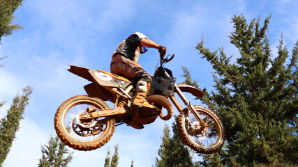 Professional dirt bike motocross rider performing stunts and flying from jump in extreme terrain...