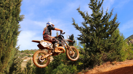 Professional dirt bike motocross rider performing stunts and flying from jump in extreme terrain...