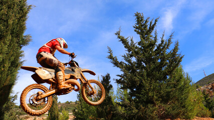 Professional dirt bike motocross rider performing stunts and flying from jump in extreme terrain...