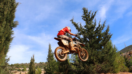 Professional dirt bike motocross rider performing stunts and flying from jump in extreme terrain...