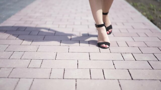 Feet of young woman in high-heeled footwear going in the city .. Female legs in high heels shoes walking in the urban street. Slow motion