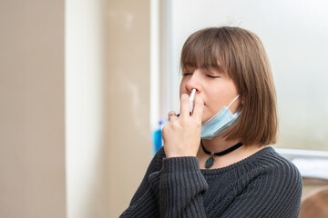 Young woman with sickness using nasal spray for protection against coronavirus while she is at work.