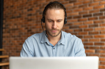Portrait of a focused millennial young businessman in a headset looking on the laptop, hipster...