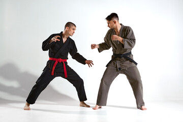 Athletic males in kimono fighting during kudo workout on white studio background with copy space, martial arts concept