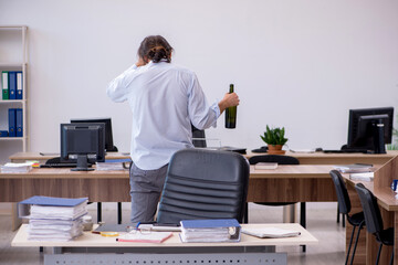 Young male employee drinking alcohol in the office