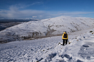 Fototapeta na wymiar girl in winter gear hiking in snow covered hills in Scotland on a bright blue day