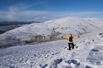 hiker girl in the snow covered hills wearing a yellow jacket and enjoying the Ochil Hills landscape