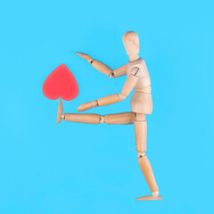 Wooden mannequin kicking red heart on blue background