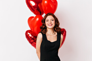 Romantic ginger girl posing with heart shaped balloons. Studio shot of lovable young woman isolated...
