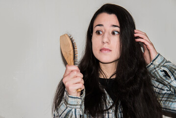 Mujer joven sujetando con la mano un cepillo con pelo caído mientras tiene una expresión de shock y sorpresa. Concepto de caída del cabello