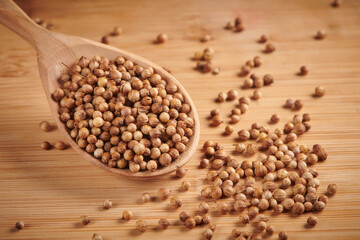 Dry coriander seeds in spoon on a wooden background. Close up view.