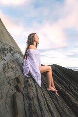 Young caucasian girl wearing only a white shirt on a rocky beach