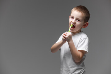 Happy child kid boy brushing teeth with toothbrush on gray background. Health care, dental hygiene. Mockup, copy space