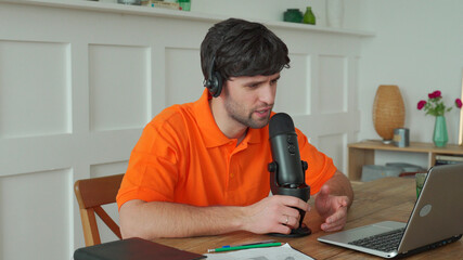 Man is speaking in microphone in studio recording podcast gesturing expressing opinions for online blog.