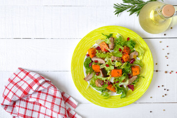Dietary salad with roast turkey, pumpkin and green lettuce on a white wooden background. Top view.