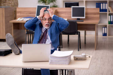 Old businessman employee in wheel-chair working in the office