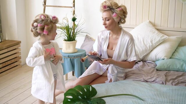young beautiful mother with her daughter in white coats in the apartment on bed