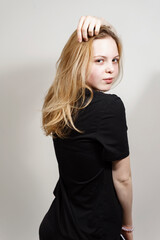 portrait of a beautiful red-haired teenager girl in a black t-shirt. the girl stands half a turn and touches her hair with her hand