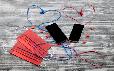 Red medical masks and two smartphones with hearts shape headphones and sweets on wooden background.