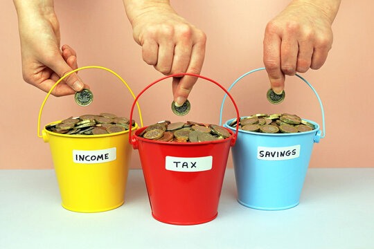 Hands Distributing Pound Coins In To Three Different Coloured Pots Labelled Income, Tax And Savings.