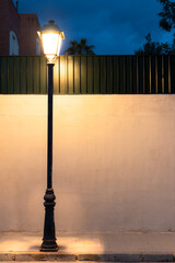 Una farola lámpara bombilla en la noche alumbrando una pared y una calle con acera con cielo azul...
