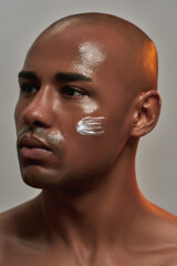 Closeup portrait of handsome young african american man with cream applied on his cheek looking away while posing isolated over gray background