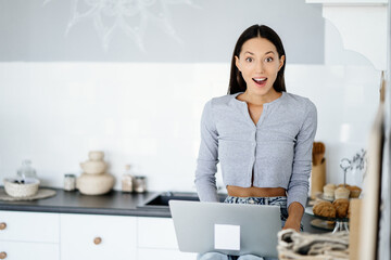 Image of cute brunette woman sitting at kitchen and using laptop