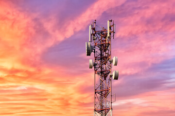 Telecommunication tower with antennas against beautiful colorful sky at sunset or dawn with pink clouds background.