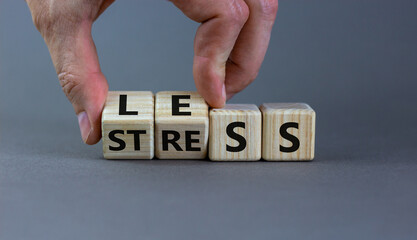 Having less stress or being stress-less. Businessman turns wooden cubes and changes the word 'STRESS' to 'LESS'. Beautiful grey background, copy space. Medical, lifestyle and less stress concept.