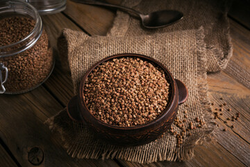 Organic uncooked scattered buckwheat grain in a bowl and glass jar on a rustic wooden background