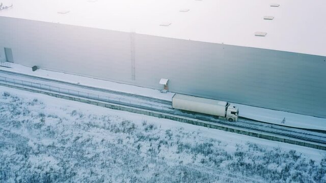 Semi-trailer truck drives along a modern warehouse in a logistics park on a winter day. Aerial view