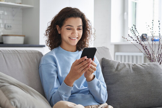 Happy hispanic teen girl holding cell phone using smartphone device at home. Smiling young latin woman blogger subscribing new social media, buying in internet, ordering products online in apps.