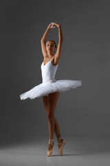 graceful ballerina in white tutu and pointe shoes dancing on gray background