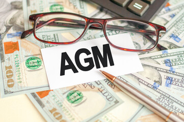 On the table are bills, a bundle of dollars and a sign on which it is written - AGM. Business and Finance concept.