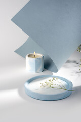 Creative composition with scented candles of soy wax in a concrete candlestick on a blue and white paper background. Eco-friendly. Minimalism. Natural. Dried flowers. Cozy shadow