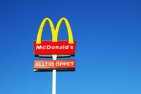 Sodertalje, Sweden - January 31, 2021: The McDonalds sign outside the hamburger restaurant with an additional sign allways open in Swedish against a blue sky.