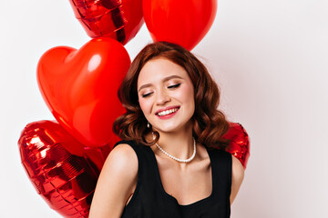 Cropped view of ginger woman laughing at party. Studio shot of caucasian girl with heart balloons.