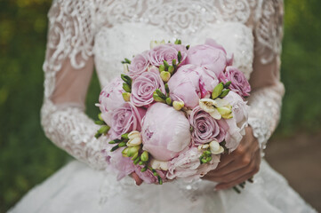 The bride stands in the garden and holds a bright wedding bouquet of peonies and roses in her hands 2669.