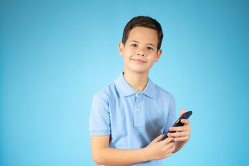 Cute ginger kid with mobile phone on blue studio background, using exciting mobile applications or chatting with friends, copy space.